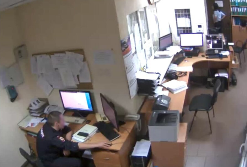 Сотруднца полиции смотрит в коридор, где располагаются двери в камеры административно задержанных | Скриншот видеозаписи с камеры видеонаблюдения в дежурной части